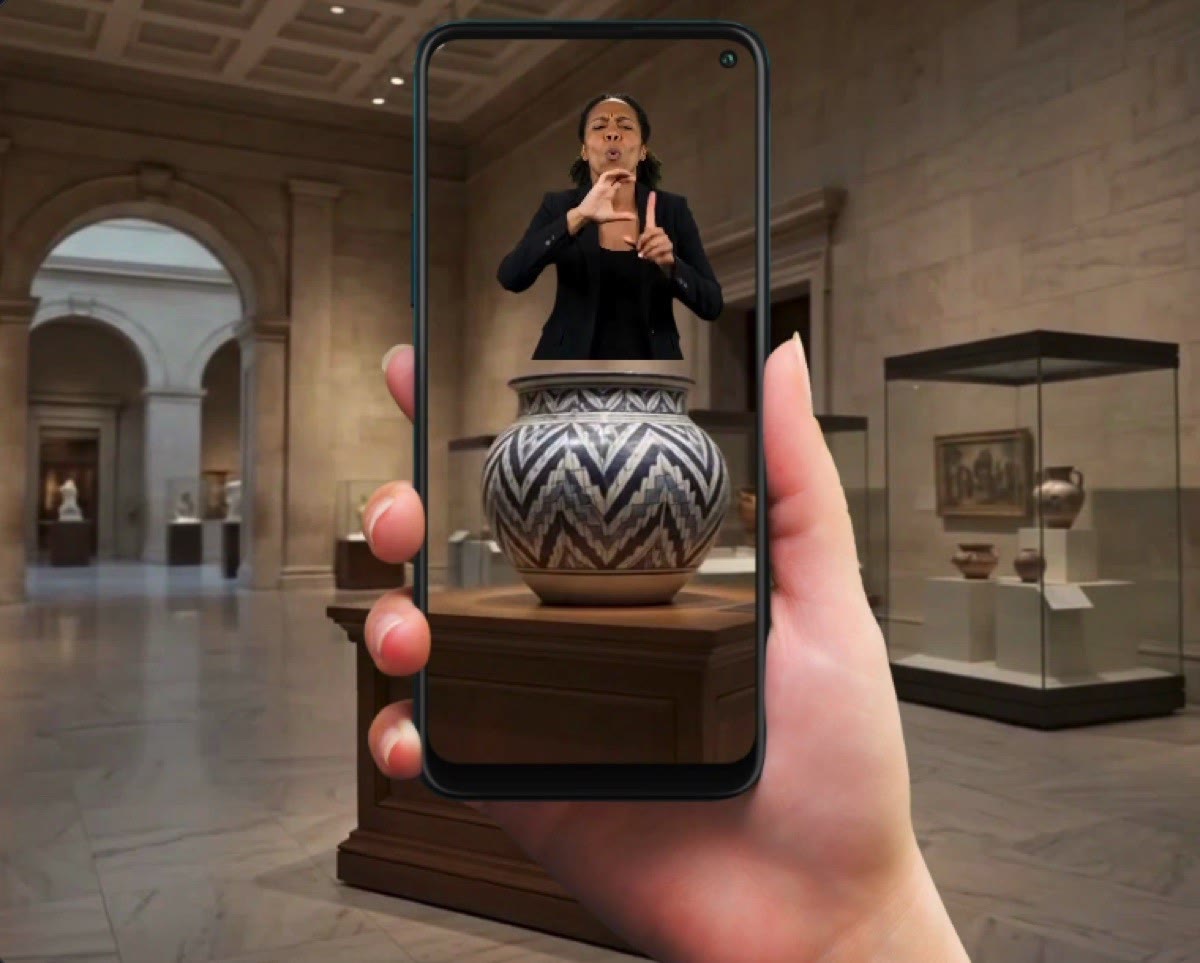 Mano con un celular en la sala de un museo; en la pantalla, una vasija con una intérprete de señas sobre ella